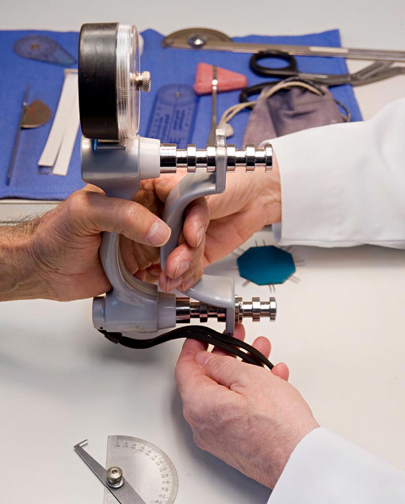 Die Hand eines Patienten umschließt ein Handdynamometer, während die Hände eines Ergotherapeuten das Gerät während der Kraftmessung anpassen.