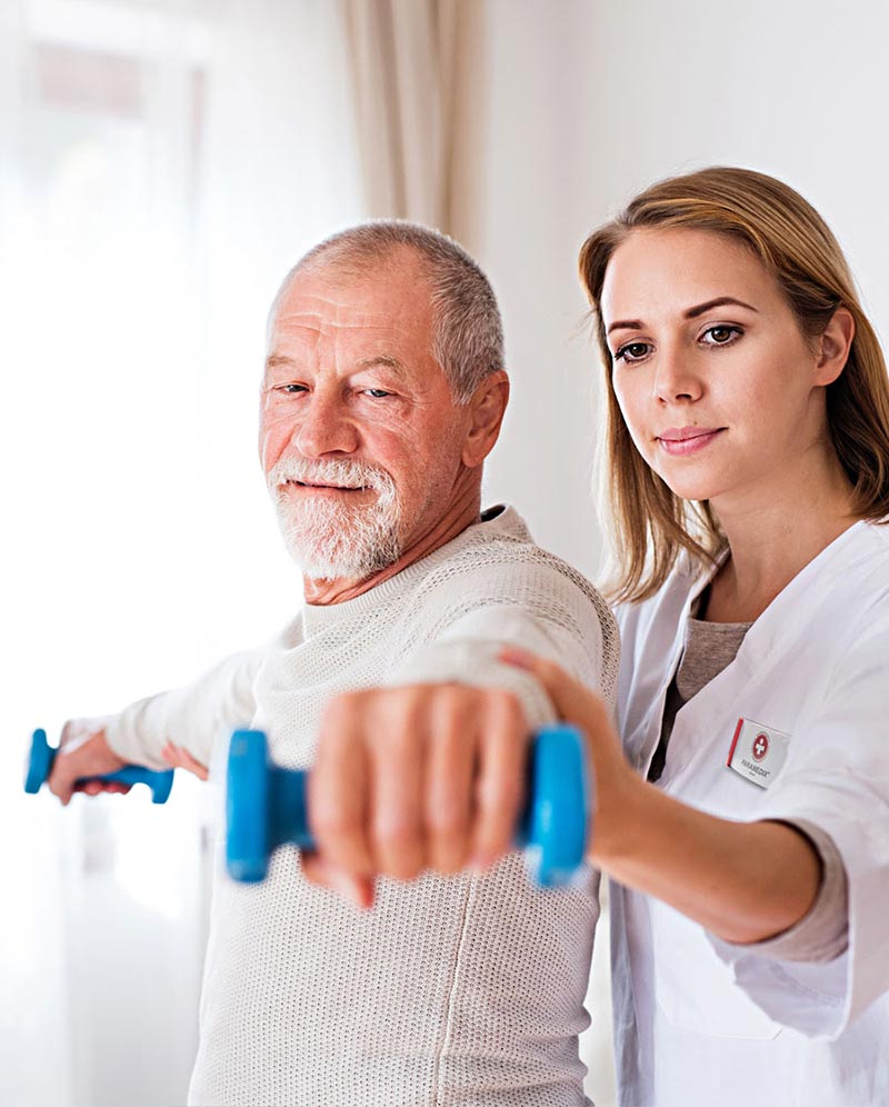 Eine Physiotherapeutin gibt Anweisungen, während ein Patient mit einer Hantel trainiert.